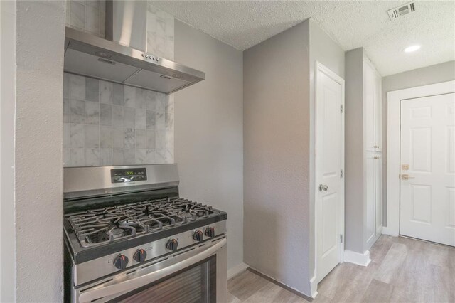 2301 N Kelham Ave, Oklahoma City, OK 73111 - kitchen with stainless steel gas stove, wall chimney range hood, tasteful backsplash, light wood-style flooring, and a textured ceiling