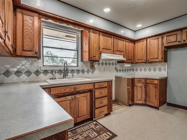 513 SW 57th St, Oklahoma City, OK 73109 - kitchen featuring brown cabinetry, a sink, under cabinet range hood, light countertops, and backsplash