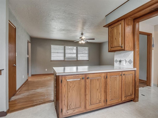513 SW 57th St, Oklahoma City, OK 73109 - kitchen with a ceiling fan, a peninsula, brown cabinetry, light countertops, and a textured ceiling