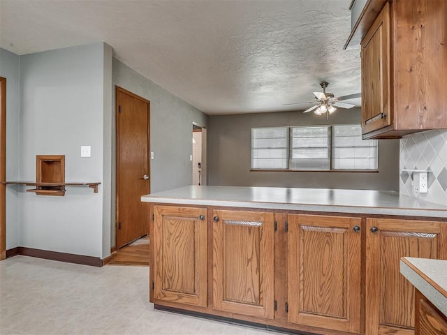 513 SW 57th St, Oklahoma City, OK 73109 - kitchen featuring brown cabinets, light countertops, a ceiling fan, a peninsula, and baseboards