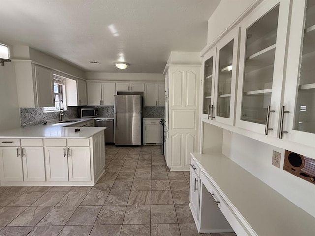 1908 NW 56th Ter, Oklahoma City, OK 73118 - kitchen featuring stainless steel appliances, backsplash, glass insert cabinets, light countertops, and a peninsula