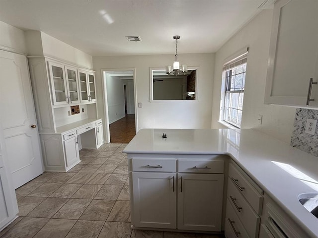1908 NW 56th Ter, Oklahoma City, OK 73118 - kitchen featuring a peninsula, a chandelier, light countertops, glass insert cabinets, and white cabinets