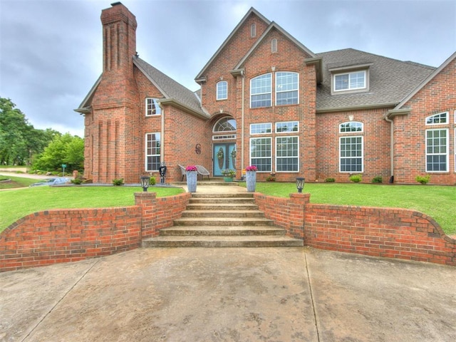 2508 Thunderwind Cir, Edmond, OK 73034 - view of front facade featuring brick siding, roof with shingles, a front lawn, and a chimney
