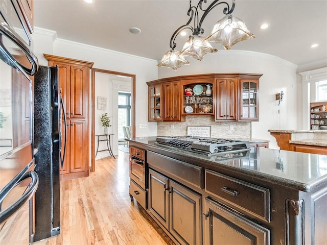 2508 Thunderwind Cir, Edmond, OK 73034 - kitchen with stainless steel gas cooktop, light wood-style floors, tasteful backsplash, glass insert cabinets, and dark stone countertops