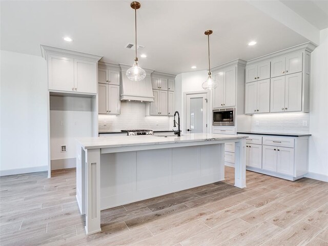 11508 NW 102nd St, Yukon, OK 73099 - kitchen featuring stainless steel microwave, custom range hood, decorative backsplash, light wood-style floors, and recessed lighting