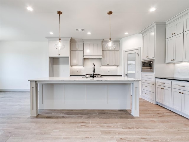 11508 NW 102nd St, Yukon, OK 73099 - kitchen featuring built in microwave, decorative backsplash, custom exhaust hood, light wood finished floors, and an island with sink