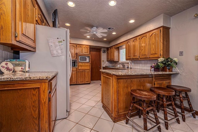 427 Foreman Ave, Norman, OK 73069 - kitchen featuring a peninsula, white appliances, brown cabinets, ceiling fan, and a textured ceiling