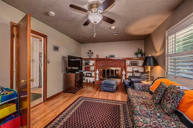 427 Foreman Ave, Norman, OK 73069 - living room with wood finished floors, a textured ceiling, a ceiling fan, and a brick fireplace