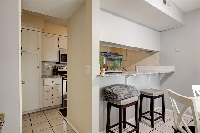 809 Cardinal Creek Blvd, Norman, OK 73072 - kitchen with stainless steel appliances, light tile patterned floors, a breakfast bar, backsplash, and light stone counters