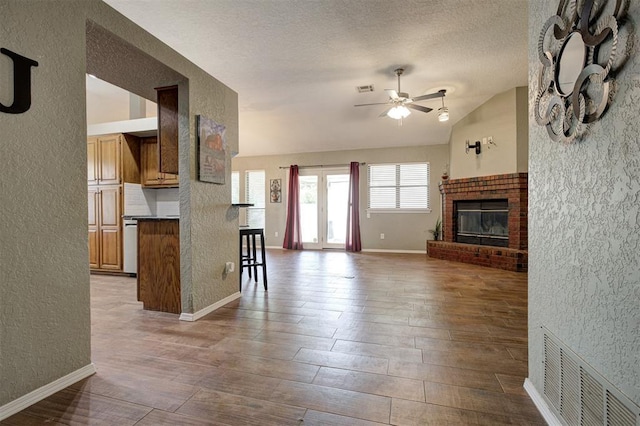 1001 Glacier Ln, Edmond, OK 73003 - living area with vaulted ceiling, a textured wall, a ceiling fan, a fireplace, and a textured ceiling