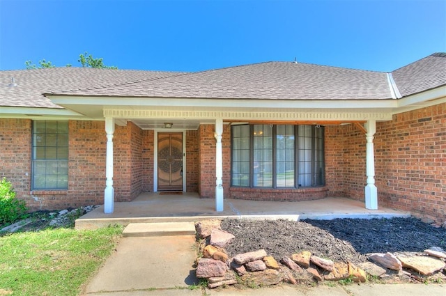 4205 Sooner Cir, Edmond, OK 73034 - doorway to property featuring a porch, brick siding, and roof with shingles
