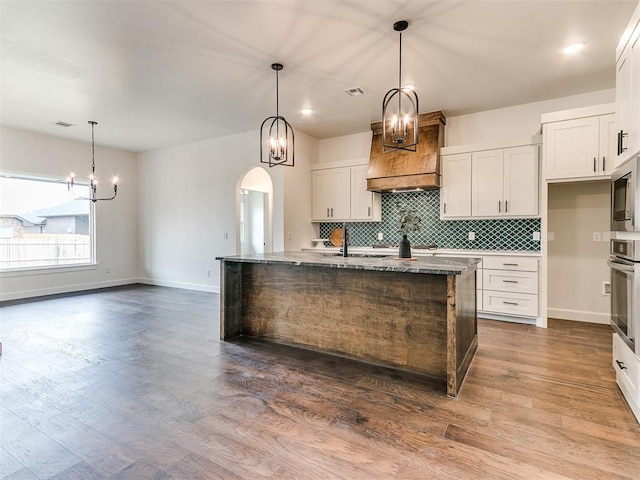 9316 NW 84th St, Yukon, OK 73099 - kitchen with a chandelier, oven, an island with sink, tasteful backsplash, and arched walkways