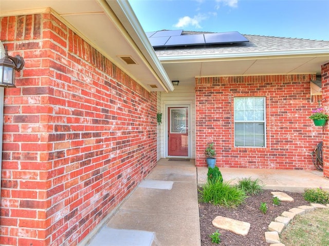 409 NW Jefferson Ave, Piedmont, OK 73078 - view of exterior entry featuring brick siding, roof mounted solar panels, and roof with shingles