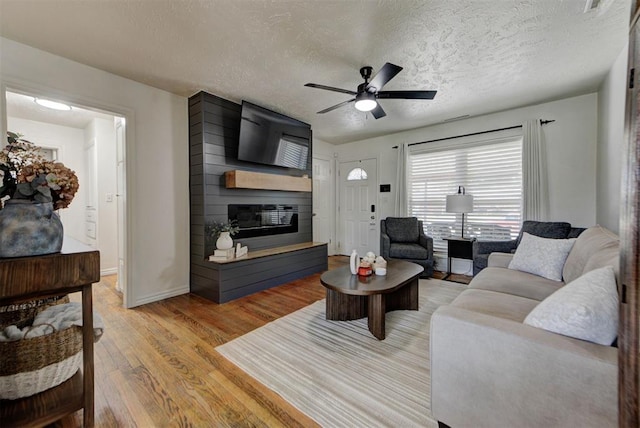 2805 SW 54th Pl, Oklahoma City, OK 73119 - living room with a large fireplace, light wood-type flooring, ceiling fan, a textured ceiling, and baseboards