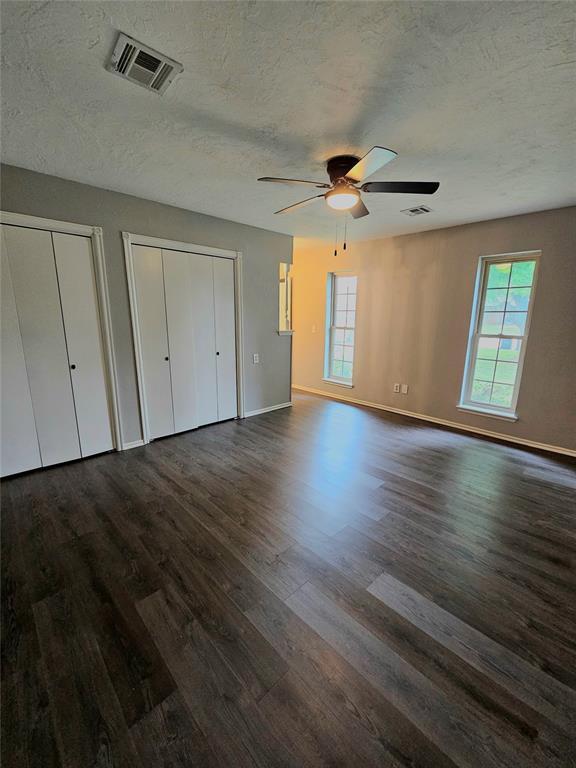 6013 Greenview Dr, Oklahoma City, OK 73135 - unfurnished bedroom featuring dark wood finished floors, multiple windows, a textured ceiling, multiple closets, and baseboards
