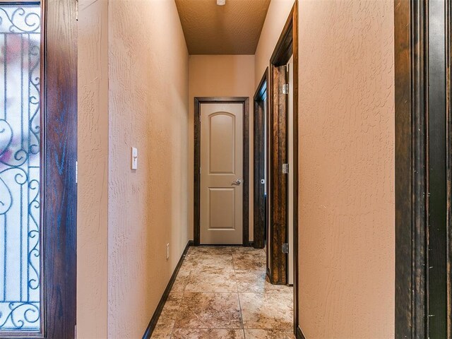 17016 Barcelona Dr, Oklahoma City, OK 73170 - corridor featuring a textured wall, baseboards, and light stone finish floors