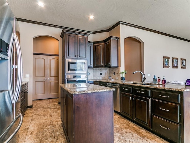 17016 Barcelona Dr, Oklahoma City, OK 73170 - kitchen featuring appliances with stainless steel finishes, arched walkways, ornamental molding, a kitchen island, and light stone countertops