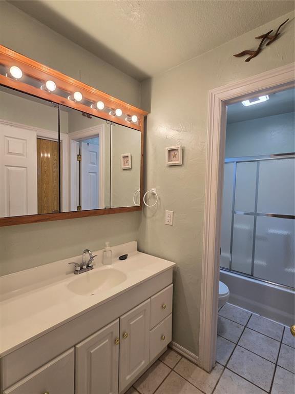 110534 S 4183rd Rd, Checotah, OK 74426 - bathroom with vanity, tile patterned flooring, a textured ceiling, shower / bath combination with glass door, and toilet
