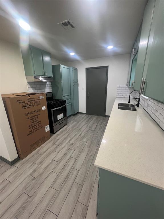 6505 NW 34th St, Bethany, OK 73008 - kitchen with gas stove, green cabinetry, a sink, light wood-style floors, and light countertops