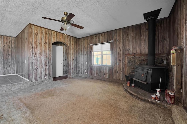 508 E Parker St, Granite, OK 73547 - unfurnished living room with a wood stove, wood walls, ceiling fan, carpet flooring, and a textured ceiling