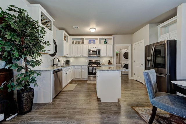11734 Split Oak Cir, Guthrie, OK 73044 - kitchen featuring appliances with stainless steel finishes, stacked washer and clothes dryer, open shelves, a center island, and white cabinets