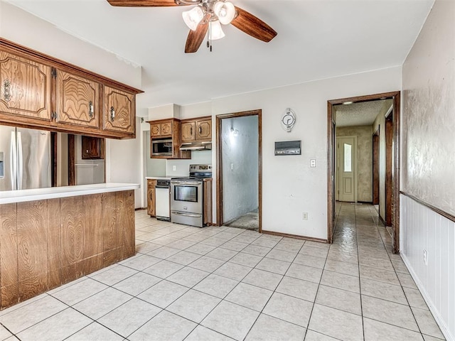 19005 Aerial Rd, Edmond, OK 73012 - kitchen featuring appliances with stainless steel finishes, under cabinet range hood, a ceiling fan, brown cabinetry, and light tile patterned floors