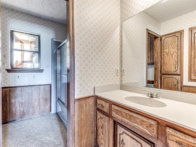 19005 Aerial Rd, Edmond, OK 73012 - bathroom with a textured ceiling, vanity, wallpapered walls, a wainscoted wall, and bath / shower combo with glass door