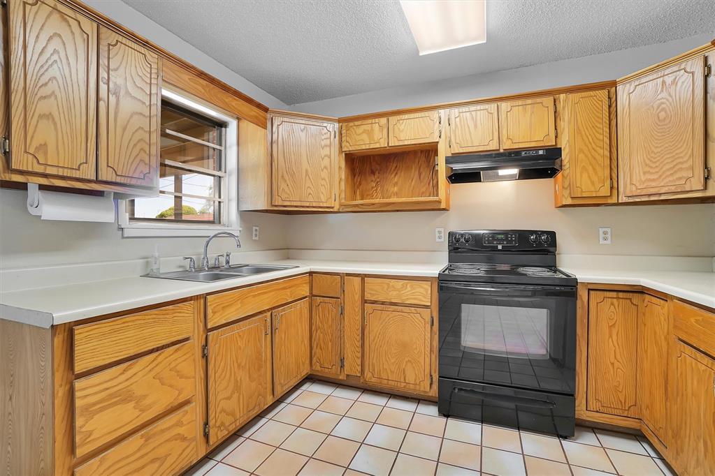 1036 Box St, Altus, OK 73521 - kitchen with under cabinet range hood, black range with electric cooktop, a sink, a textured ceiling, and light countertops