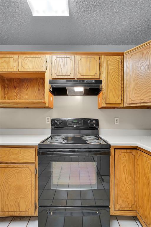 1036 Box St, Altus, OK 73521 - kitchen with electric range, under cabinet range hood, a textured ceiling, light countertops, and tile patterned flooring