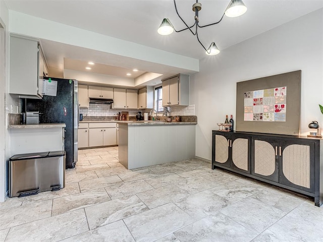 13613 Pin Oak, Edmond, OK 73013 - kitchen with a tray ceiling, under cabinet range hood, backsplash, a peninsula, and a chandelier