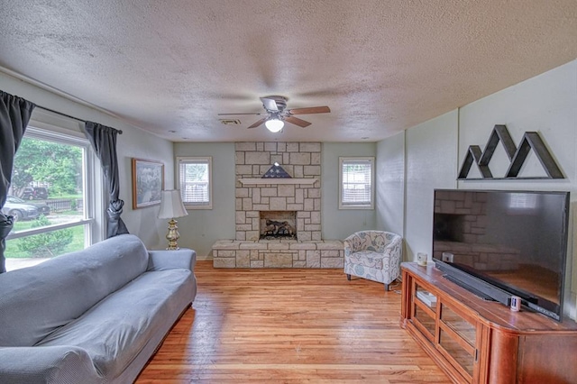 912 E Comanche St, Norman, OK 73071 - living area featuring a fireplace, a textured ceiling, light wood-style flooring, and ceiling fan