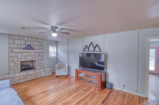 912 E Comanche St, Norman, OK 73071 - living area featuring a textured ceiling, wood finished floors, a ceiling fan, a stone fireplace, and baseboards