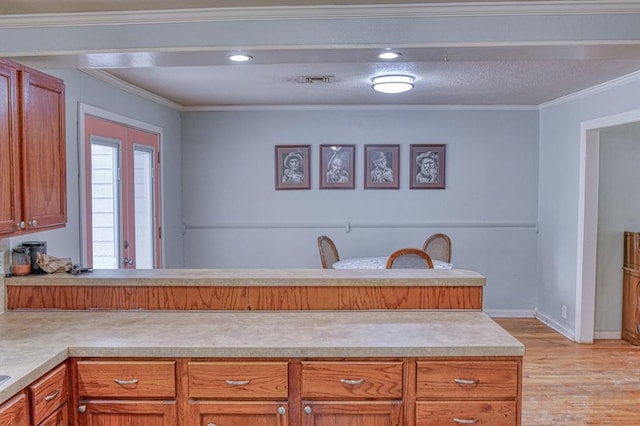 912 E Comanche St, Norman, OK 73071 - kitchen with light countertops, light wood-style floors, a peninsula, ornamental molding, and brown cabinets