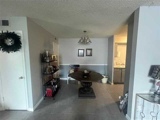 tiled dining space with a chandelier, a textured ceiling, a sink, and baseboards