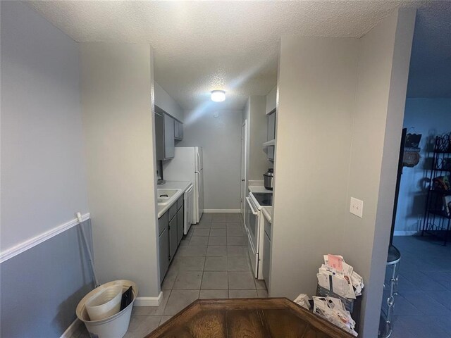kitchen featuring a textured ceiling, light tile patterned floors, white appliances, light countertops, and gray cabinets
