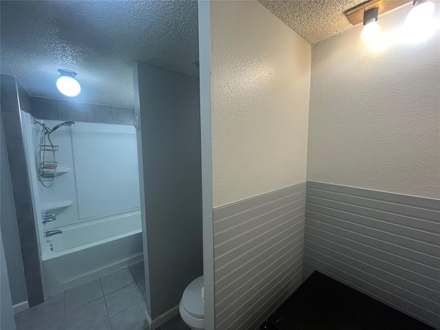 full bath with a textured ceiling, toilet, tile patterned floors, wainscoting, and shower / tub combination