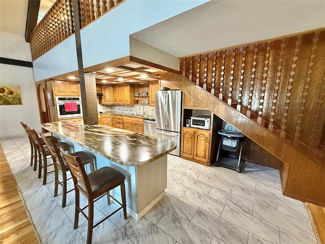 129 Park Dr, Sayre, OK 73662 - kitchen featuring stainless steel appliances, a kitchen bar, brown cabinetry, and dark countertops