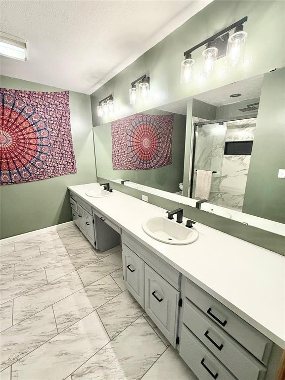 129 Park Dr, Sayre, OK 73662 - bathroom featuring marble look tile flooring, double vanity, a shower stall, and a textured ceiling