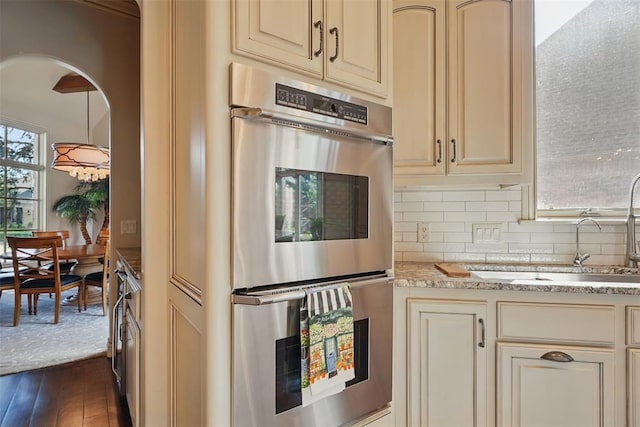 15005 Dourdan Ct, Oklahoma City, OK 73142 - kitchen with cream cabinetry, stainless steel double oven, a sink, tasteful backsplash, and light stone counters