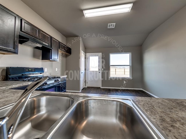 3909 S Ravine St, Stillwater, OK 74074 - kitchen with gas range, under cabinet range hood, dark wood-type flooring, dark brown cabinetry, and lofted ceiling