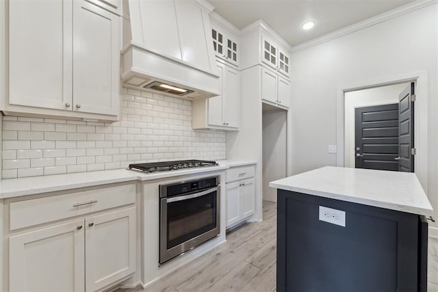 18813 Windy Way Rd, Edmond, OK 73012 - kitchen with appliances with stainless steel finishes, custom exhaust hood, tasteful backsplash, light wood-style flooring, and white cabinetry