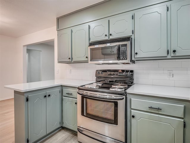 4709 Wilcox Ln, Yukon, OK 73099 - kitchen featuring stainless steel appliances, a peninsula, light wood finished floors, decorative backsplash, and light countertops