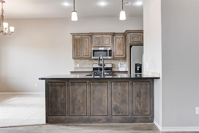 7720 Hawk Ln, Guthrie, OK 73044 - kitchen with stainless steel appliances, backsplash, hanging light fixtures, dark brown cabinetry, and baseboards