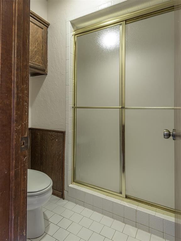 13501 Fox Hollow Rdg, Oklahoma City, OK 73131 - full bath with toilet, a shower with door, a textured wall, and tile patterned flooring