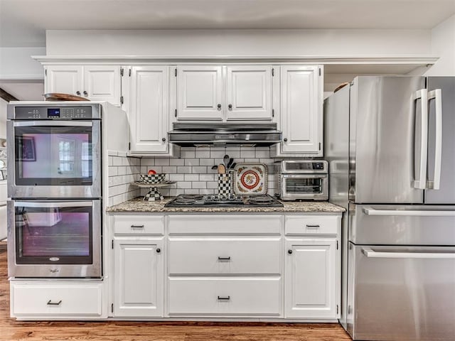 2009 Bella Vista Dr, Edmond, OK 73013 - kitchen with stainless steel appliances, under cabinet range hood, white cabinets, light stone counters, and decorative backsplash