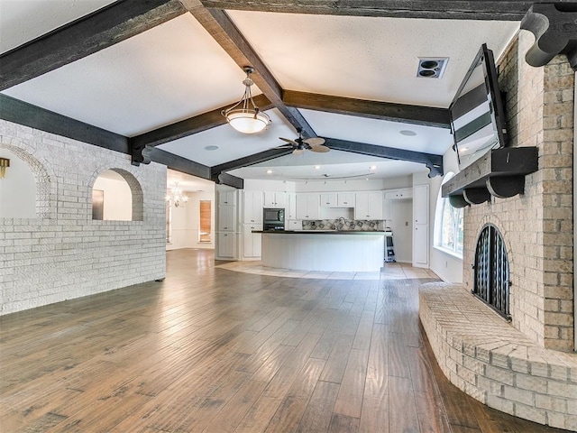 212 W Ridgewood Dr, Midwest City, OK 73130 - unfurnished living room featuring ceiling fan, beam ceiling, light wood-style flooring, a brick fireplace, and brick wall