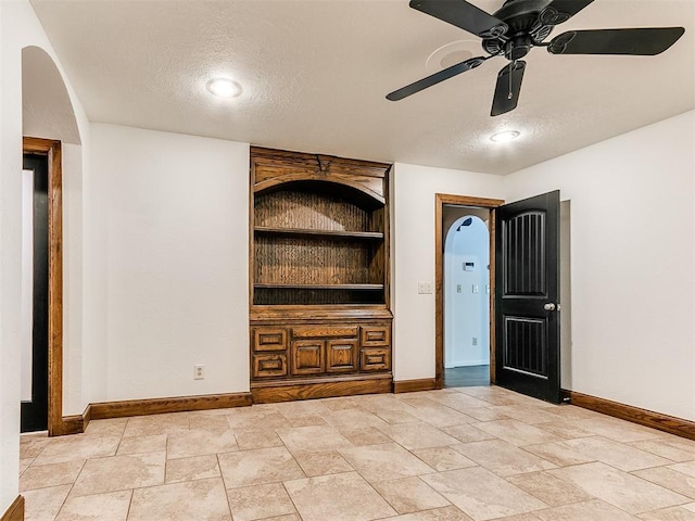 212 W Ridgewood Dr, Midwest City, OK 73130 - unfurnished living room featuring baseboards, a textured ceiling, built in features, a ceiling fan, and arched walkways