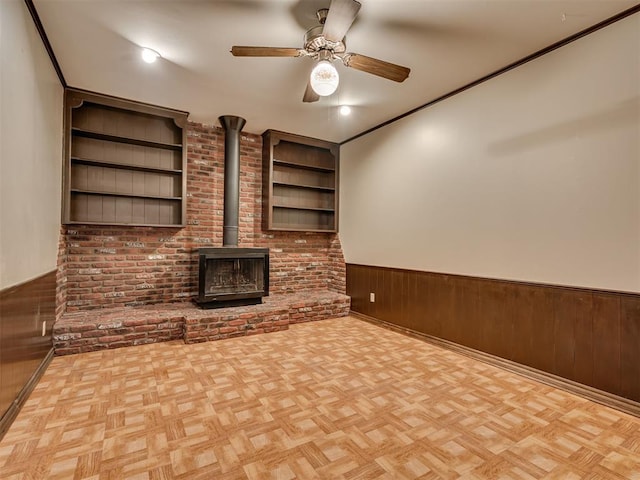 4809 N Pate Ave, Oklahoma City, OK 73112 - unfurnished living room featuring a wood stove, wainscoting, ceiling fan, wooden walls, and built in features