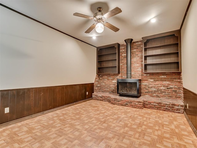 4809 N Pate Ave, Oklahoma City, OK 73112 - unfurnished living room featuring a ceiling fan, a wood stove, a wainscoted wall, wood walls, and brick wall