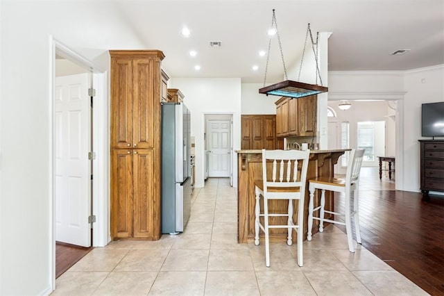 2632 SE 97th St, Moore, OK 73160 - kitchen with freestanding refrigerator, brown cabinets, a breakfast bar area, crown molding, and a peninsula